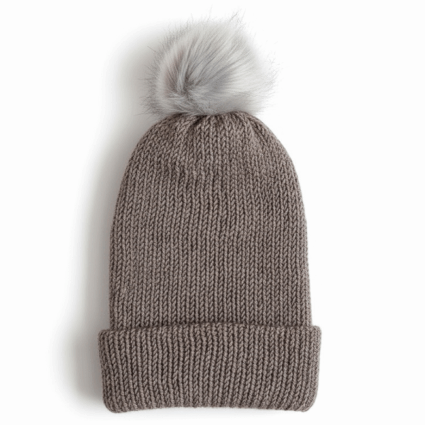 A taupe knit beanie with a light gray faux fur pom on top, displayed on a white background